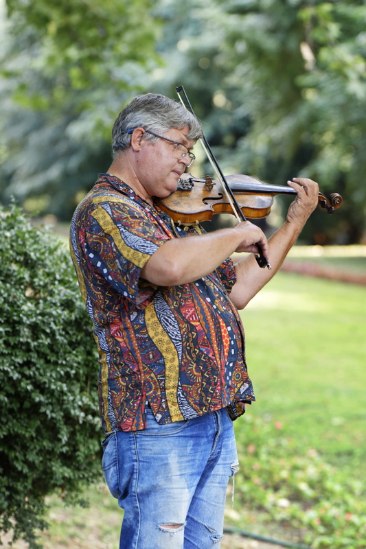 16 - A person playing the violin outdoors while wearing a patterned short-sleeved shirt and blue jeans